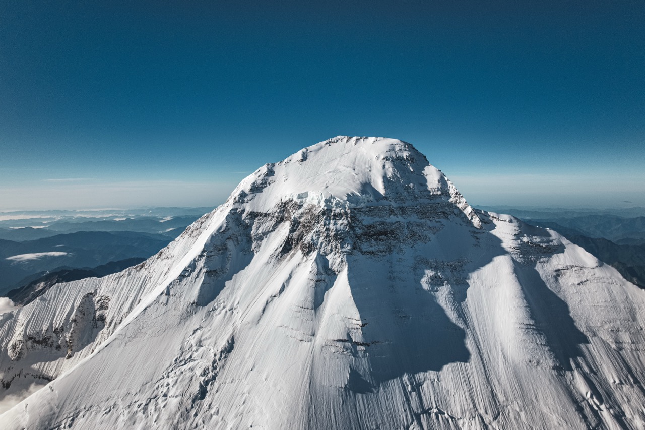 An aerial view of a snow-covered summit above the foothills